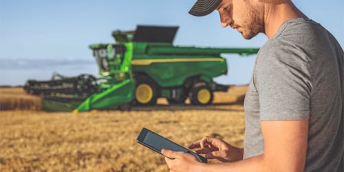 A Koenig Equipment intern using a tablet in front of a John Deere combine
