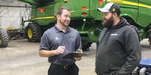 Two Koenig Equipment team members talking beside a John Deere combine