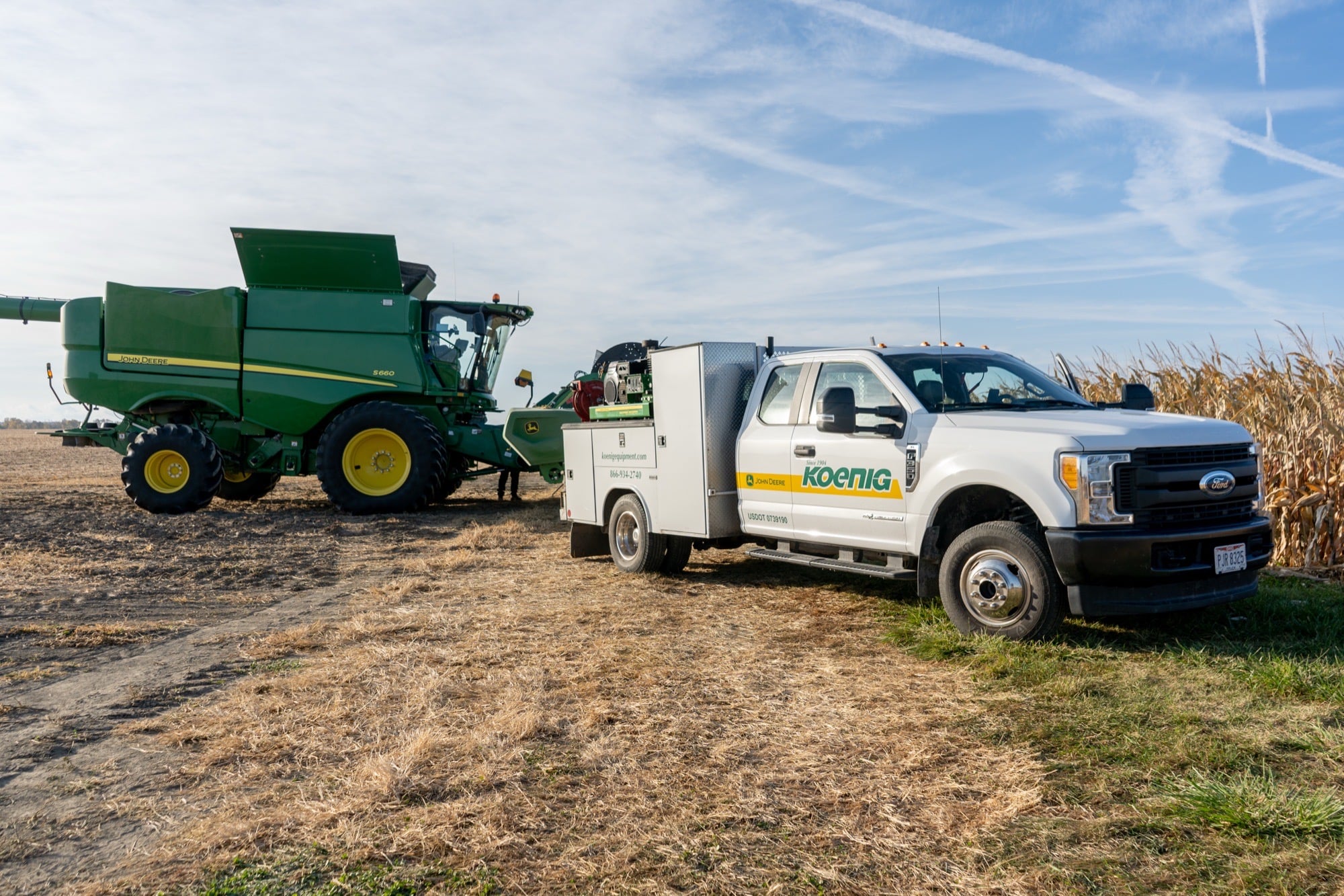 A Koenig Equipment mobile service truck parked beside a John Deere combine in a harvested field