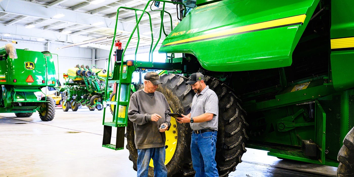 Two Koenig Equipment team members reviewing a tablet beside a John Deere combine in the service shop