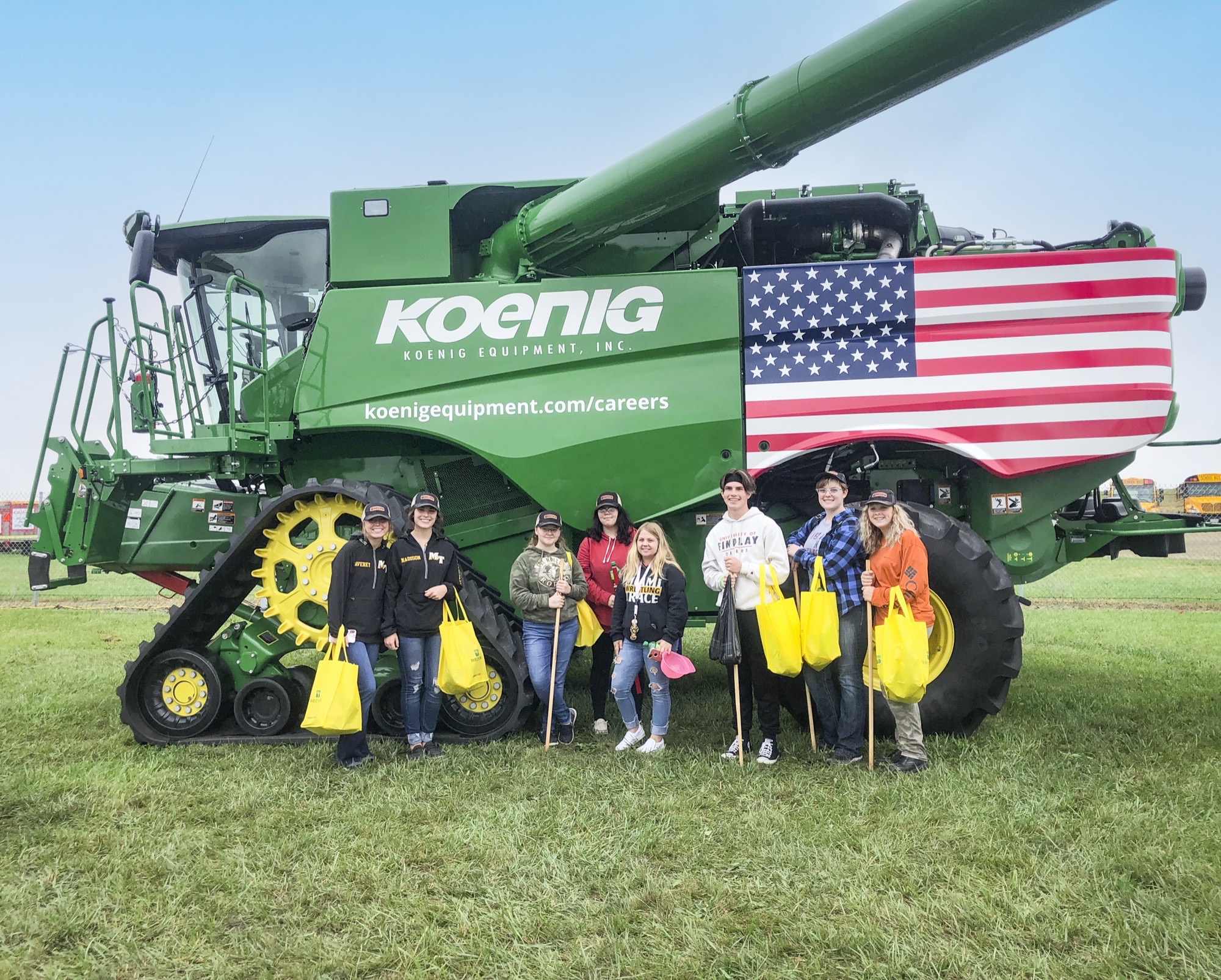 Students standing in front of a Koenig Equipment combine wrapped with an American flag and the Koenig careers web address
