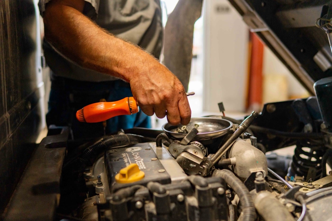 Close-up of a Koenig technician's hands working on a John Deere engine with a screwdriver