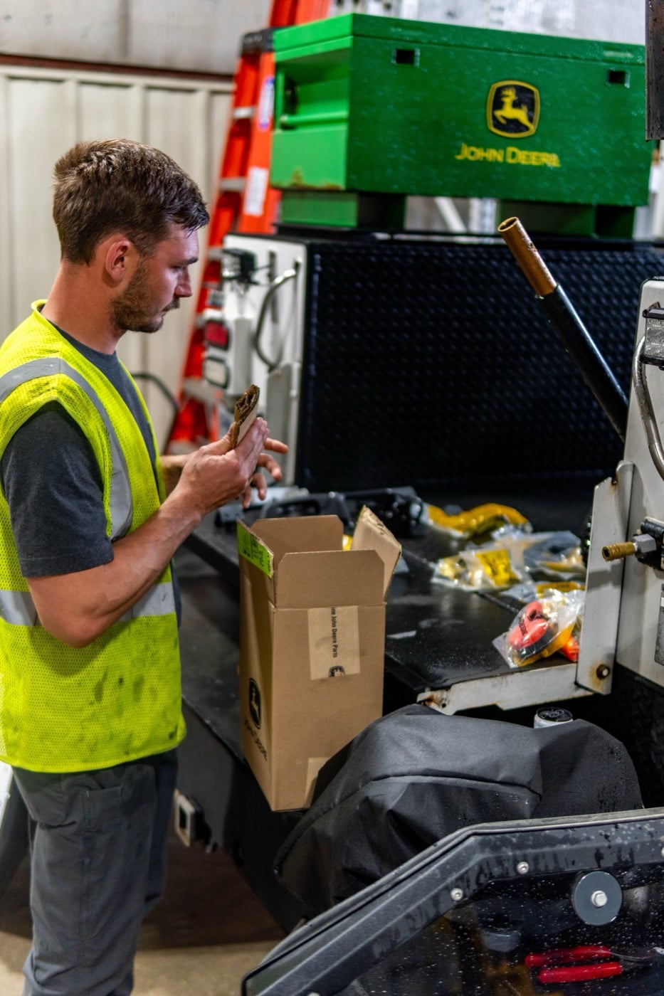 A Koenig Equipment technician inspecting a part at his service truck, with a John Deere toolbox behind him