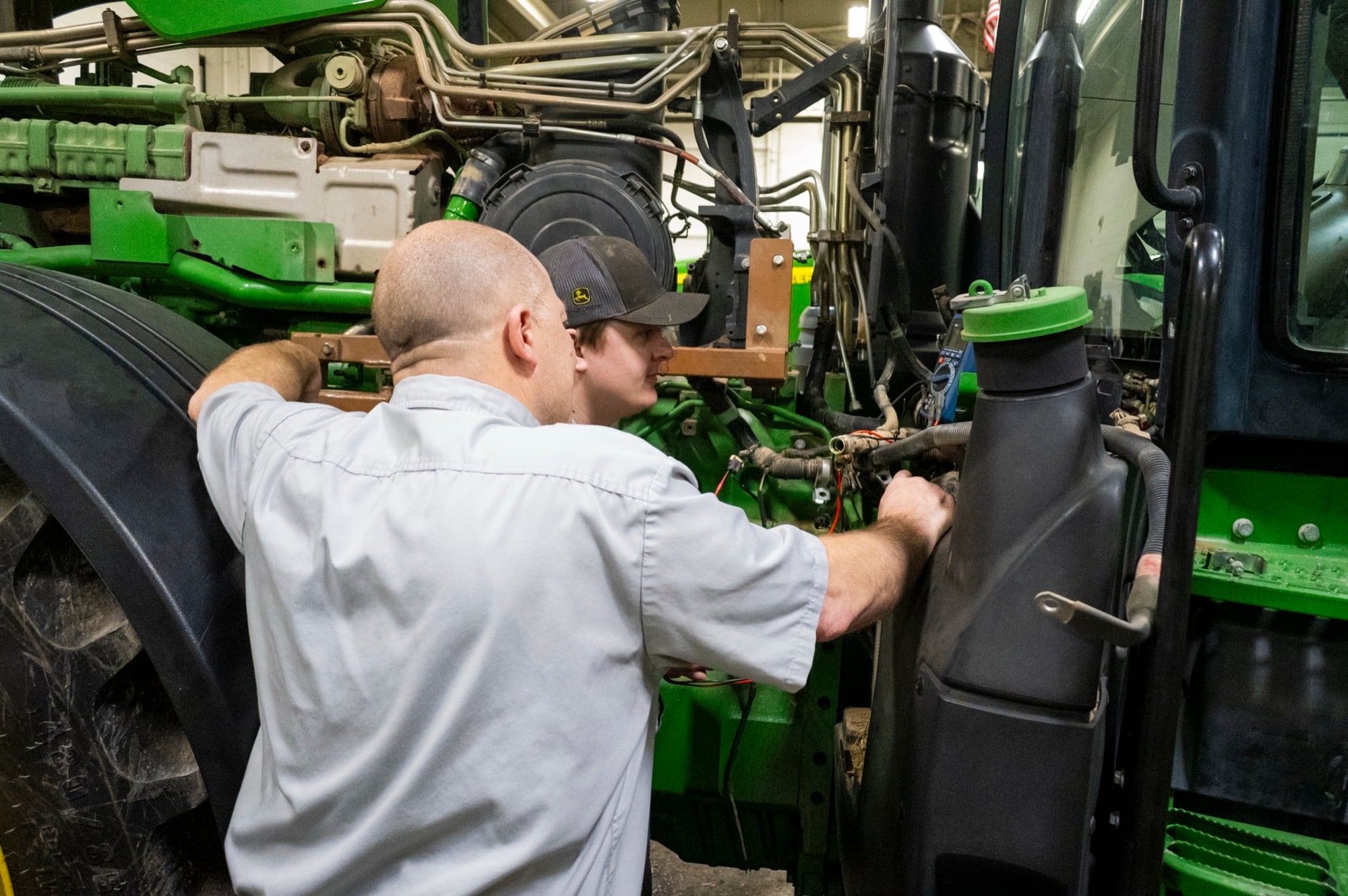 A veteran Koenig Equipment technician working alongside a younger technician on a John Deere tractor engine