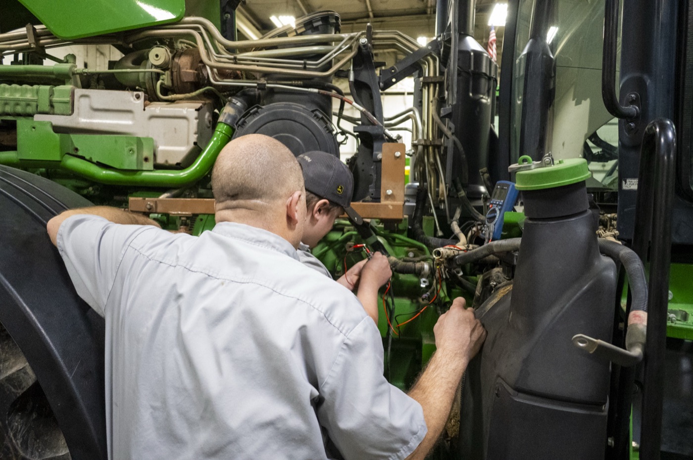 An experienced Koenig Equipment technician and a younger technician working on a John Deere tractor engine together