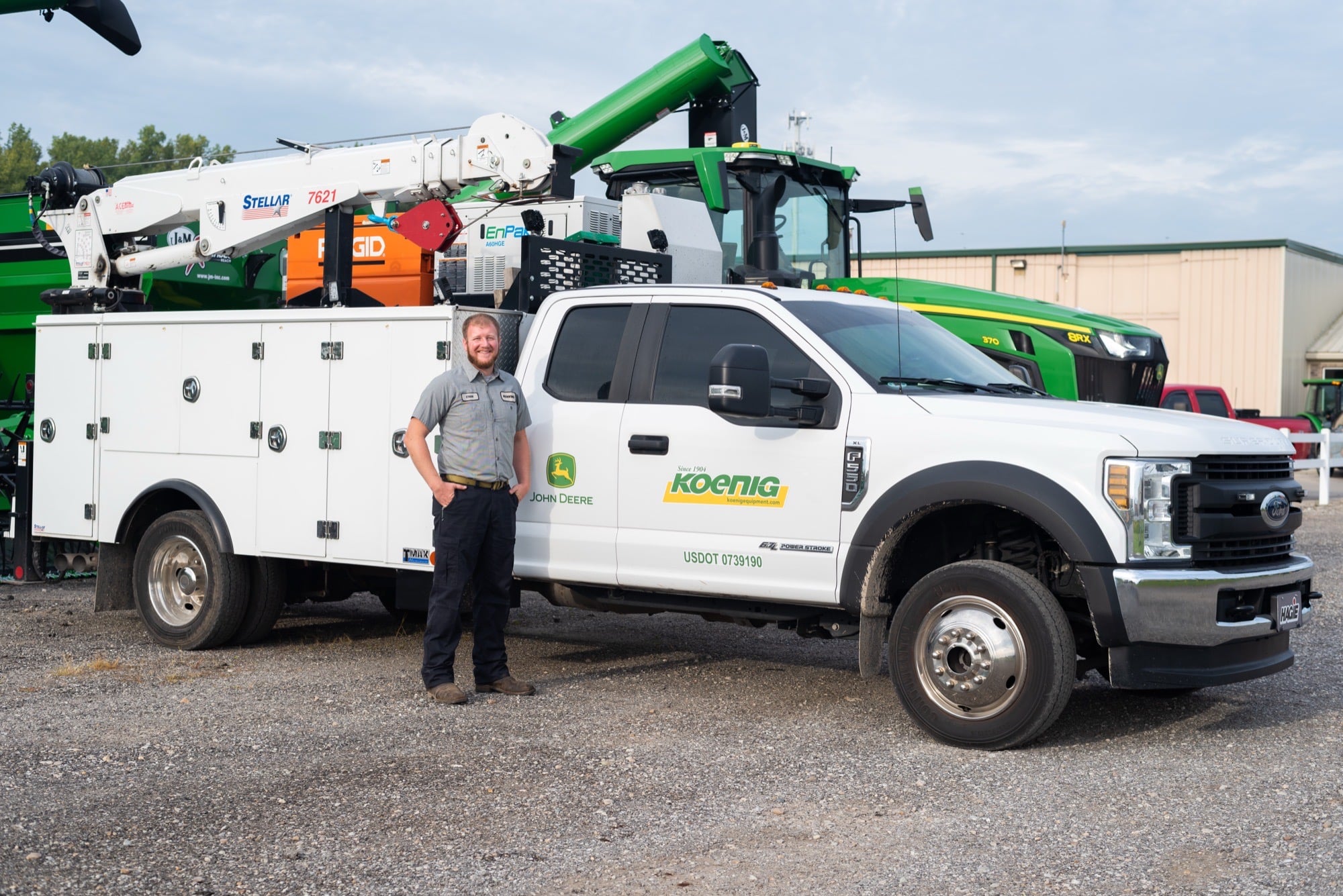 A smiling Koenig Equipment technician standing beside his mobile service truck on the dealership lot
