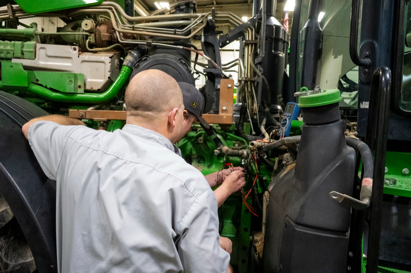 A Koenig technician tracing wiring on a John Deere tractor engine in the service shop