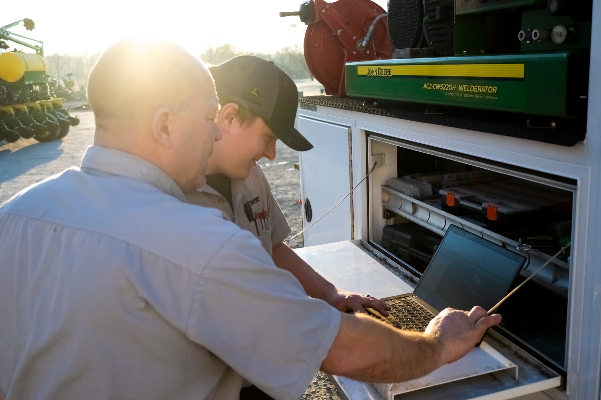 An experienced Koenig Equipment technician coaching a younger technician through diagnostics on a laptop at a service truck