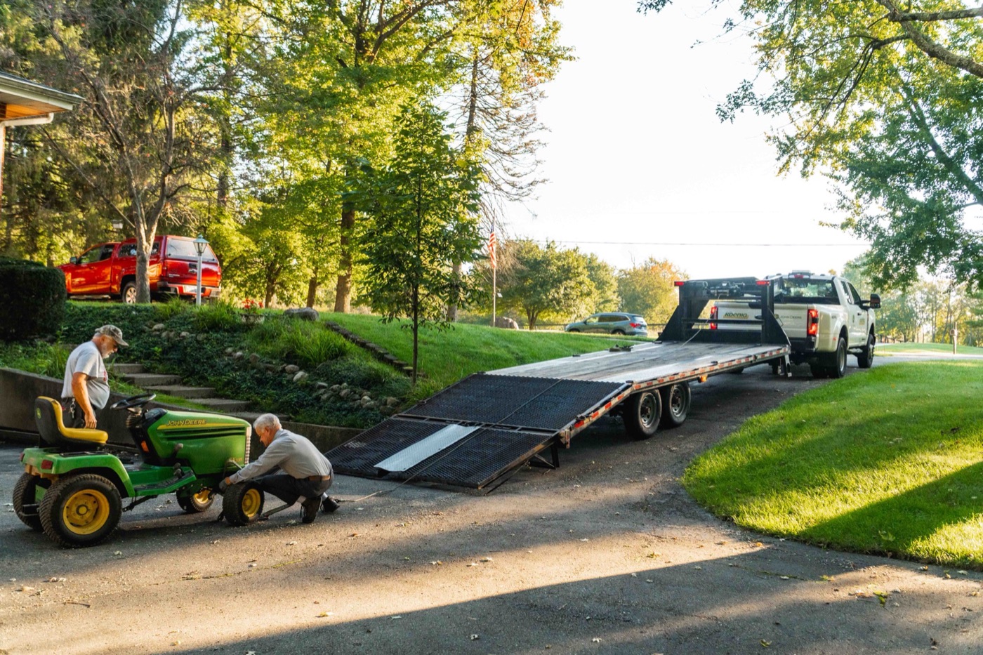Koenig Equipment team members unloading a John Deere riding mower from a trailer in a Customer's driveway